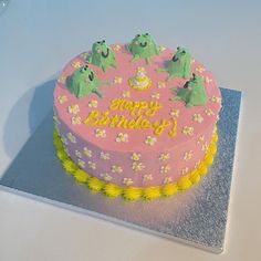 a pink birthday cake with green frogs on it