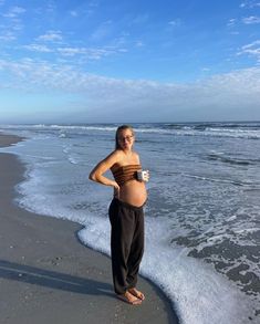 a pregnant woman standing on the beach next to the ocean