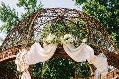 a gazebo with white flowers and greenery on the top is decorated for an outdoor wedding