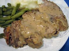 a white plate topped with meat and gravy next to green beans