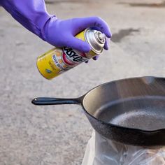 a person in purple gloves is holding a can and frying pan