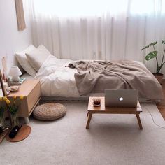 a laptop computer sitting on top of a wooden table next to a bed in a bedroom