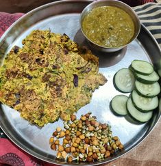 a metal plate topped with cucumbers, beans and other foods next to a bowl of sauce