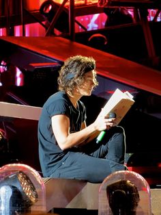 a man sitting on top of a stage reading a book