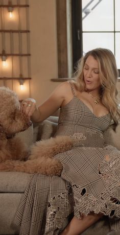 a woman in a dress sitting on a couch with a teddy bear next to her