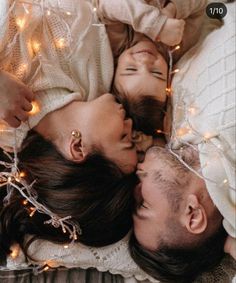 three people laying on top of each other with lights strung all around them and smiling at the camera