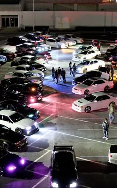 a parking lot filled with lots of cars and people walking around it at night time