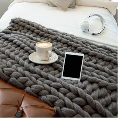 a cup of coffee, tablet and headphones on a bed with a gray blanket