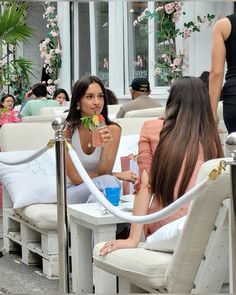 two women sitting on white chairs with drinks in their hands and one woman standing behind them