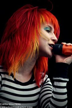 a woman with bright red hair and green eyes is singing into a microphone in front of a black background