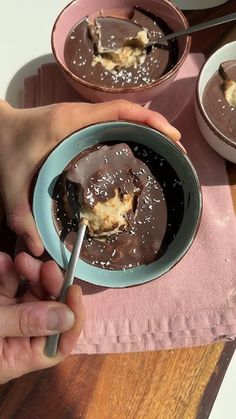 a person is holding a spoon over a bowl of chocolate pudding