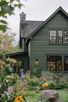 a green house with lots of windows and flowers in the front yard, surrounded by greenery