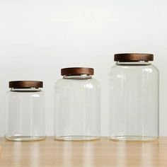 three glass jars with wooden lids on a table