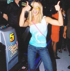 a woman standing in front of a video game machine giving the thumbs up sign with her right hand