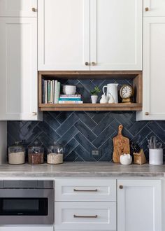 a kitchen with white cabinets and gray tile backsplash, wooden shelf over the stove