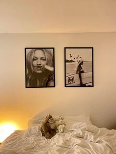 two pictures hang on the wall above a bed with white sheets and pillows, along with a teddy bear