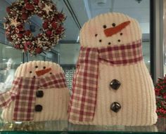 two knitted snowmen sitting next to each other on a shelf in front of a wreath