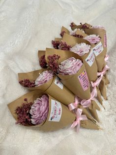 several bouquets of flowers wrapped in brown paper on a white blanket with pink ribbons