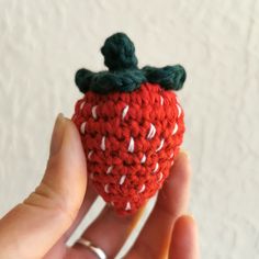 a hand holding a tiny crocheted strawberry