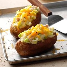 two baked potatoes on a baking sheet with a spatula