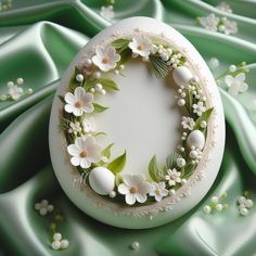 an egg decorated with flowers and leaves on a green satin table cloth, surrounded by white eggs