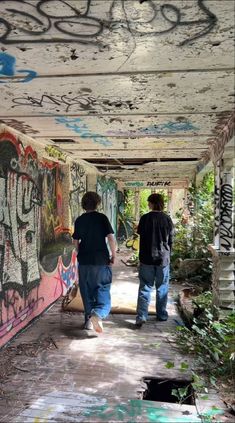 two men are walking through an abandoned building with graffiti all over the walls and ceiling