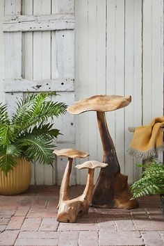 three wooden mushrooms sitting on top of a brick floor next to a potted plant