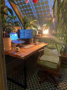 a desk with two computers on it in front of a window and potted plants