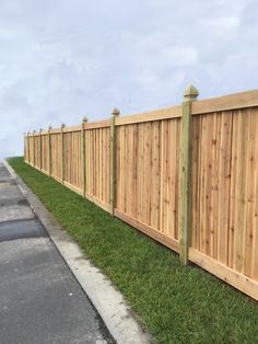 a wooden fence along the side of a road with grass growing between it and a sidewalk