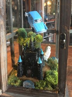 a toy car is sitting on top of a castle in a glass case with moss