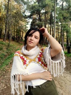 a woman is standing in the woods with her hands on her head and wearing a shawl