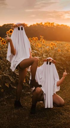 two women dressed up as ghost and sunflowers in a field with the sun setting behind them