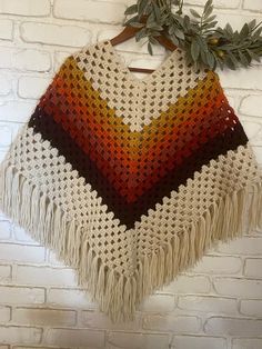 a crocheted shawl hanging on a brick wall next to a wooden hanger