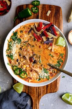 a white bowl filled with mexican food on top of a wooden cutting board next to limes