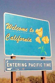 a welcome to california sign with yellow flowers in the foreground and a blue sky background