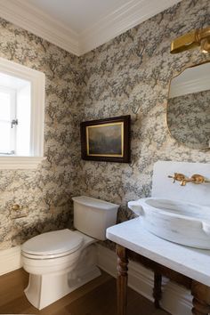 a white toilet sitting next to a sink in a bathroom under a mirror on top of a wall