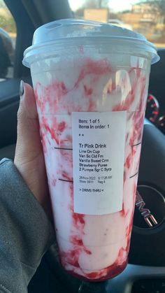 a person holding up a plastic cup with red liquid in it's wrapper