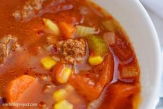 a close up of a bowl of soup with carrots, corn and ground beef