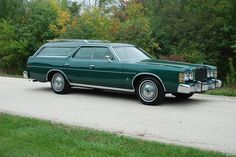 a green station wagon is parked on the side of the road in front of some trees