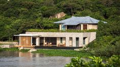 a house on the side of a river surrounded by lush green trees and greenery