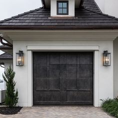 a white house with a black garage door and brick walkway leading to the front entrance