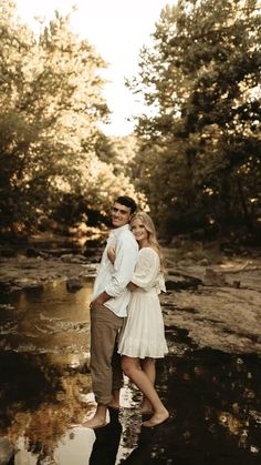 a man and woman standing next to each other in the water with trees behind them