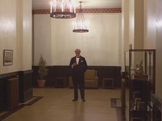 a man in a suit and bow tie standing in a room with chandeliers