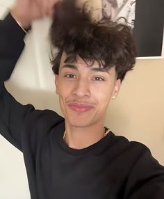 a young man wearing a black shirt is smiling and holding his hair in the air