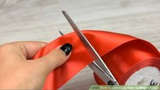 someone using scissors to cut the ribbon on a piece of red fabric with black tips