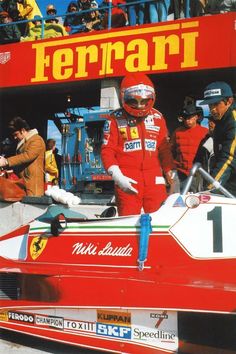 a man standing in front of a race car with people watching from the sidelines