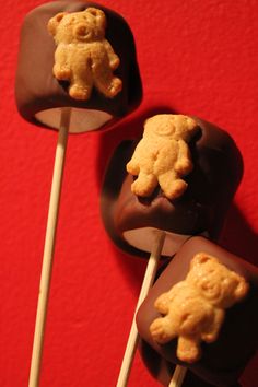 three chocolate lollipops with teddy bears on them sitting on a red surface