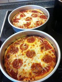 two pizzas sitting in pans on top of a stove