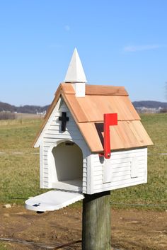 a white birdhouse with a red door and roof on a post in front of a grassy field