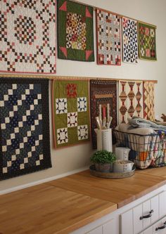 several quilts are hanging on the wall above a counter in a room with white cabinets and drawers